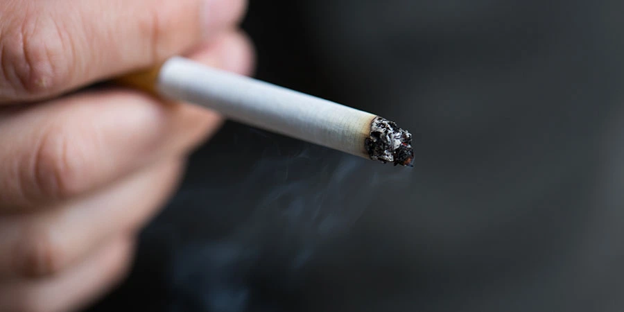 A man holding a cigarette with a hormone chart in the background.